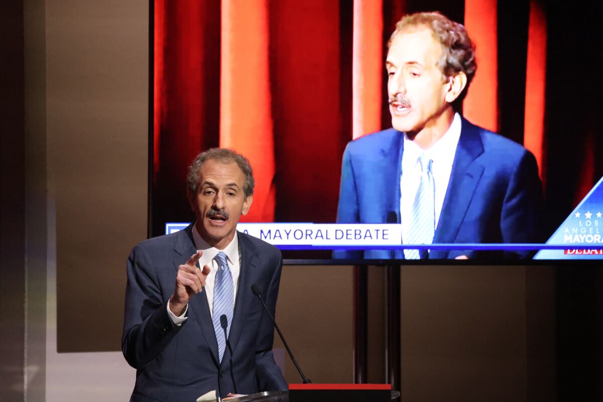 City Atty. Mike Feuer speaks at a lectern, with his image projected behind him.