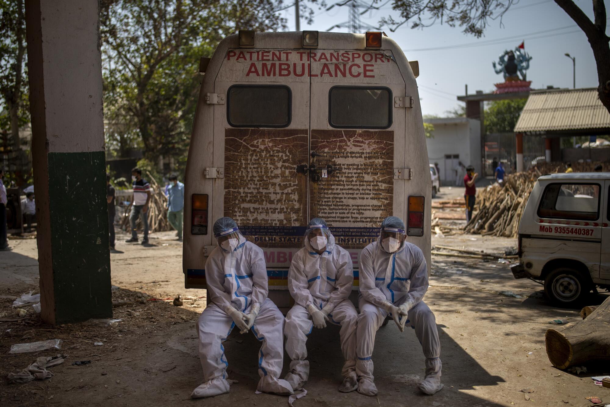 Three men sit beside an ambulance.