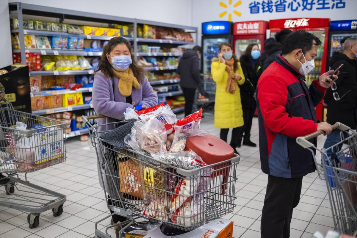 En esta foto del 22 de enero de 2020, clientes con cubrebocas hacen compras en una verdulería en Wuhan, China. La cuarentena debido al brote de coronavirus complica la logística de enviar alimentos y otros bienes a 50 millones de chinos. (AP Foto/Arek Rataj)