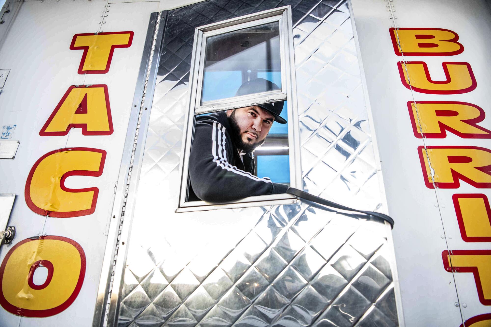 A man looks through the window of a door of a taco truck.