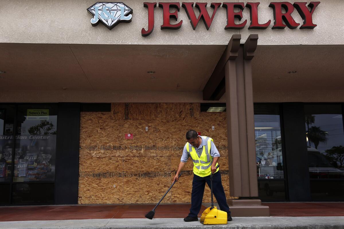 Maintenance worker Rodrigo Alonso cleans up broken glass littering the sidewalk and parking lot in front of J&L Jewelry in Long Beach.