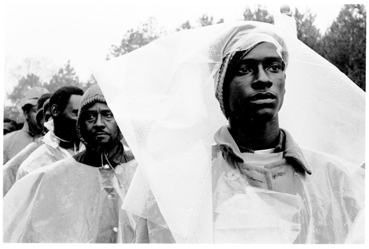 A black-and-white image of people wearing rain gear and marching in the rain.