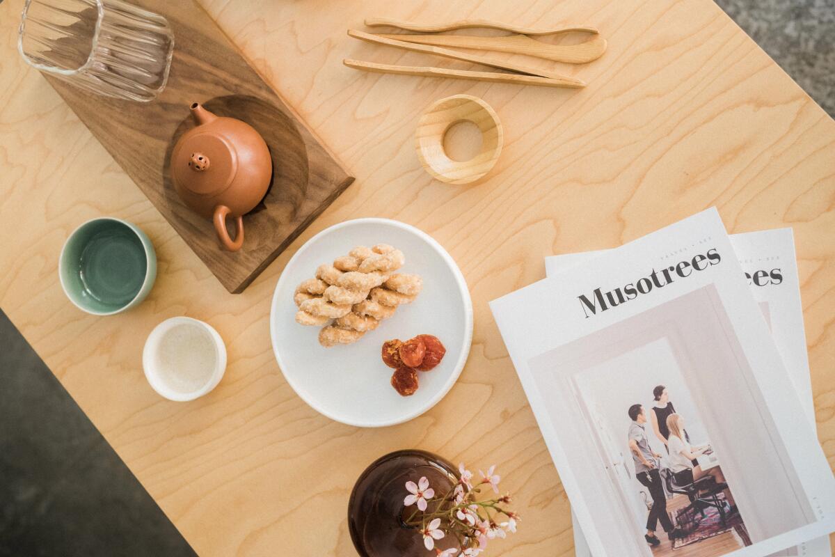 An overhead shot of a tea spread with pastries, dried fruit, a vase with flowers and magazines