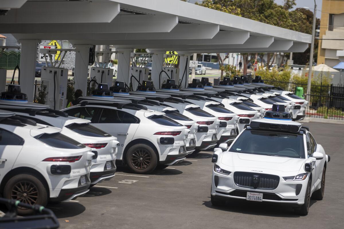 A row of white self-driving vehicles at charging ports.