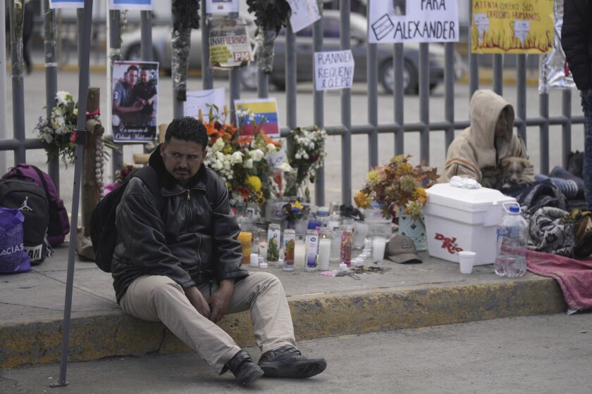 A Venezuelan migrant sits on the sidewalk where an altar was created with candles and photos outside the Mexican immigration detention center that was the site of a deadly fire, as migrants wake up after spending the night on the sidewalk in Ciudad Juarez, Mexico, Thursday, March 30, 2023. (AP Photo/Fernando Llano)