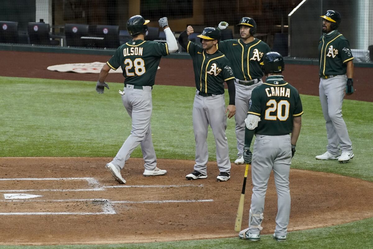Oakland Athletics' Matt Olson (28) celebrates with Tommy La Stella, second from left rear, Ramon Laureano and Marcus Semien, right rear, as Mark Canha (20) looks watches after Olson hit a grand slam off Texas Rangers' Luis Garcia during the first inning of a baseball game in Arlington, Texas, Friday, Sept. 11, 2020. (AP Photo/Tony Gutierrez)
