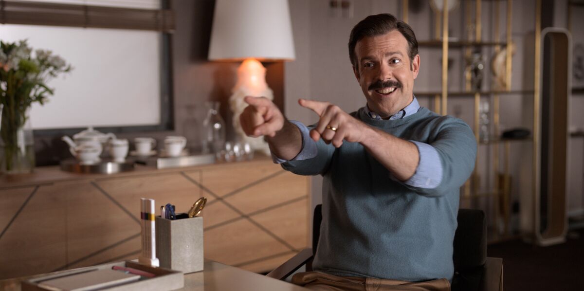 Jason Sudeikis as Ted Lasso wearing a sweater and pointing