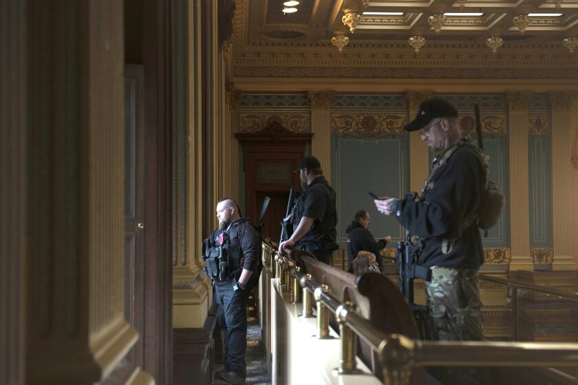 FILE - In this April 30, 2020, file photo, armed members of a militia group watch the protest outside while waiting for the Michigan Senate to vote at the Capitol in Lansing, Mich. Michigan has banned the open carry of guns in the state Capitol a week after an armed mob rioted in the U.S. Capitol and following an attempt to storm the statehouse last year. (Nicole Hester/MLive.com/Ann Arbor News via AP File)