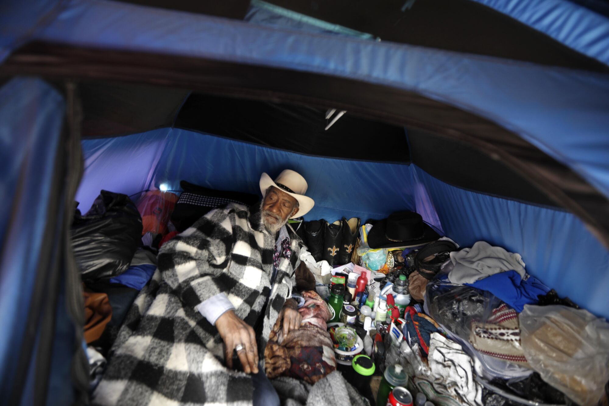 한 노인이 소지품을 들고 천막 안에서 쉬고 있습니다.