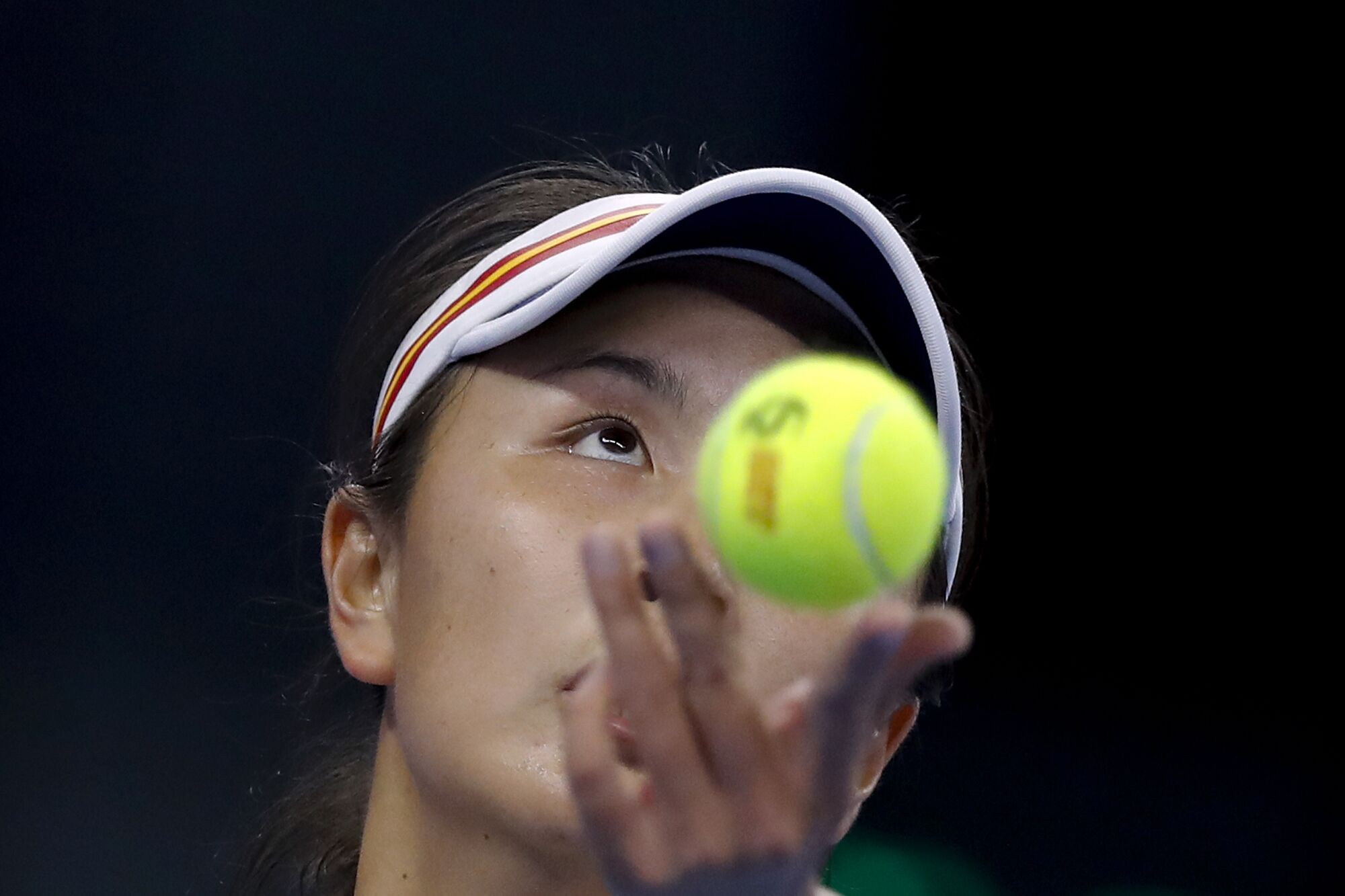 A person with a visor holds up a yellow tennis ball 