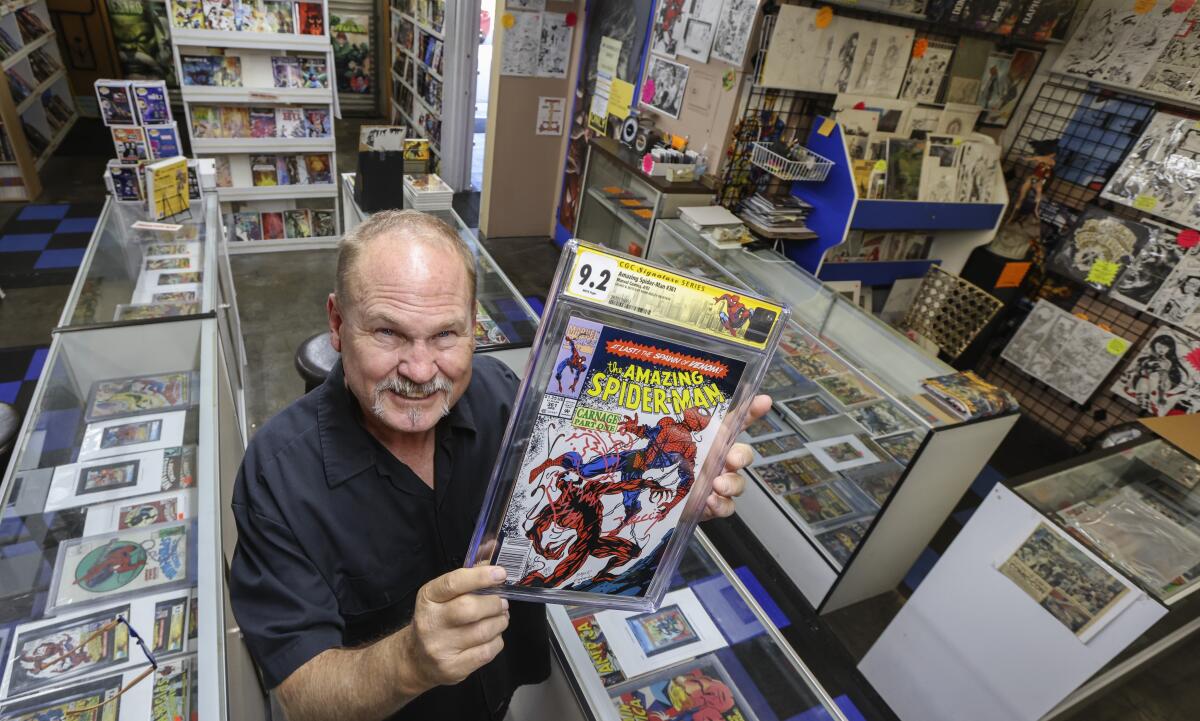 A man in a comic book store holds up a copy of "The Amazing Spiderman" in a plastic sleeve
