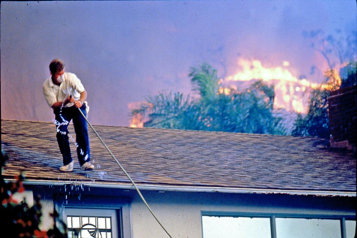 The son of homeowners pulls a garden hose to thwart advancing fire in Emerald Bay during the Laguna Beach wildfires of 1993.