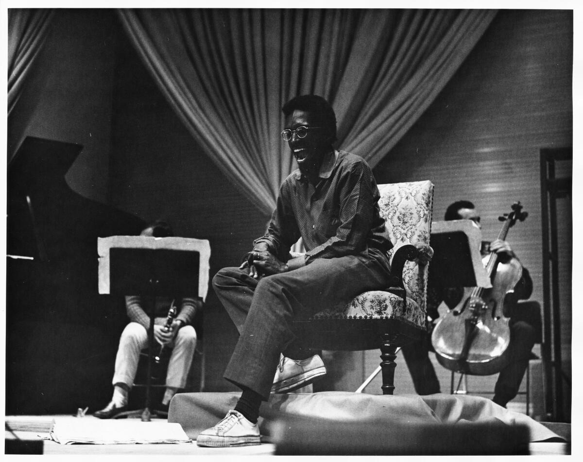  Julius Eastman seated in an armchair with instrumentalists around him.