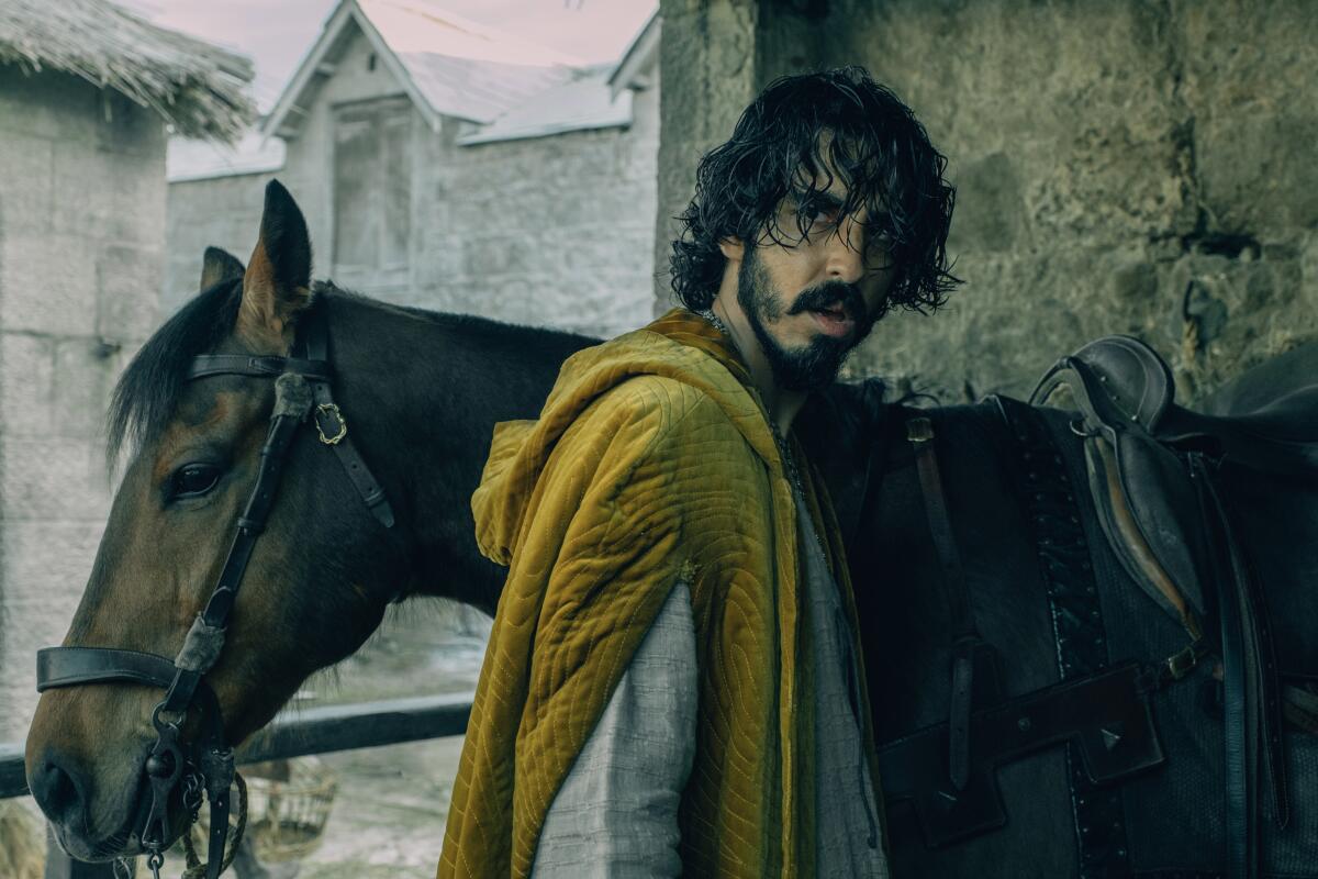 A man in medieval clothing with a horse in the movie "The Green Knight."