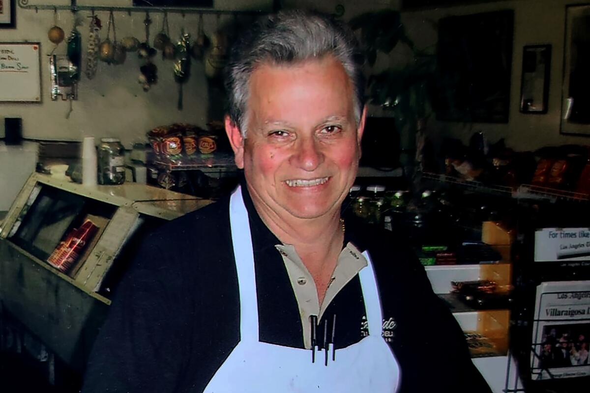 Johnny Angiuli stands behind a wooden counter. Two bottles of wine are atop the counter.