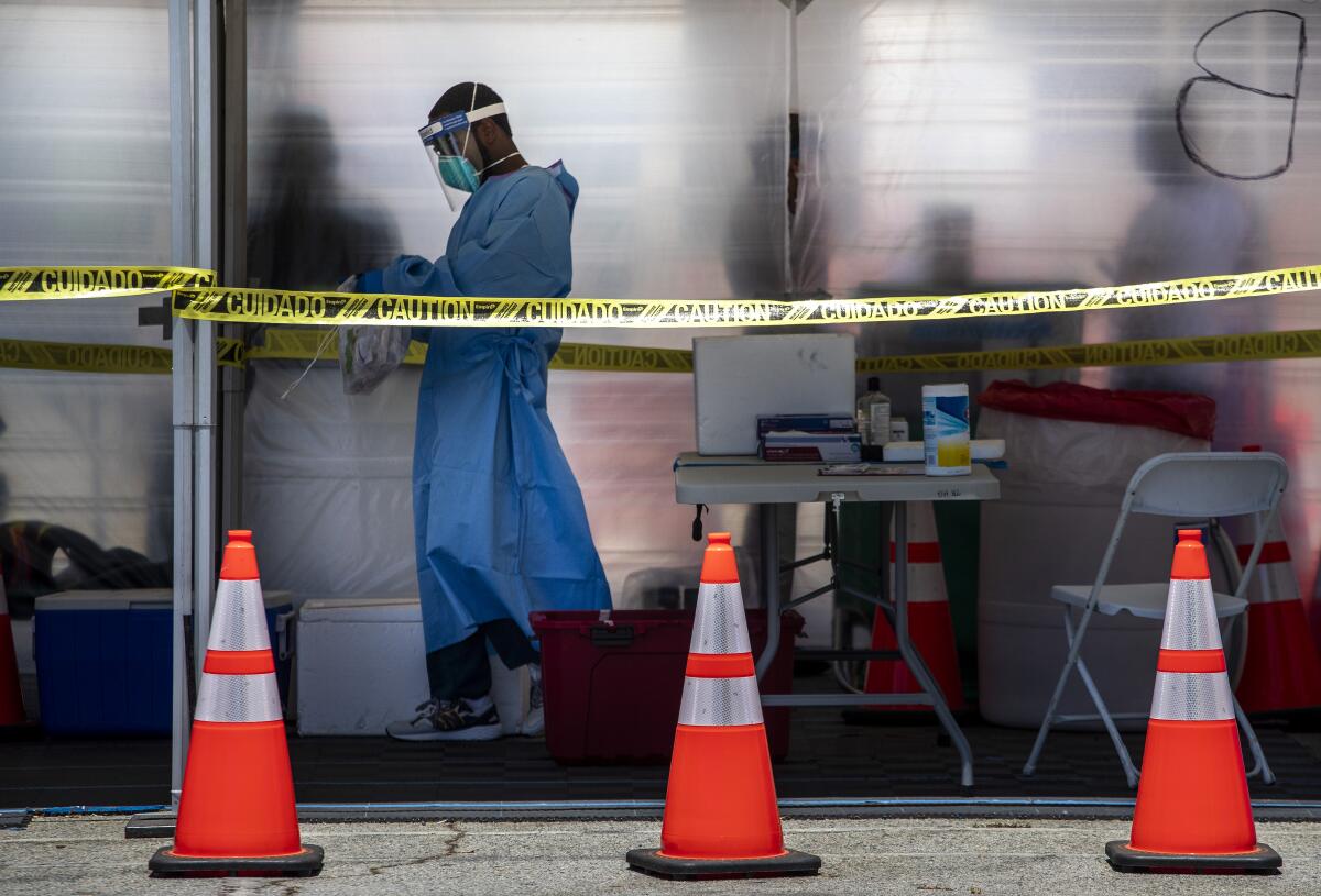 A person in protective gear carries a plastic bag in a tent behind caution tape