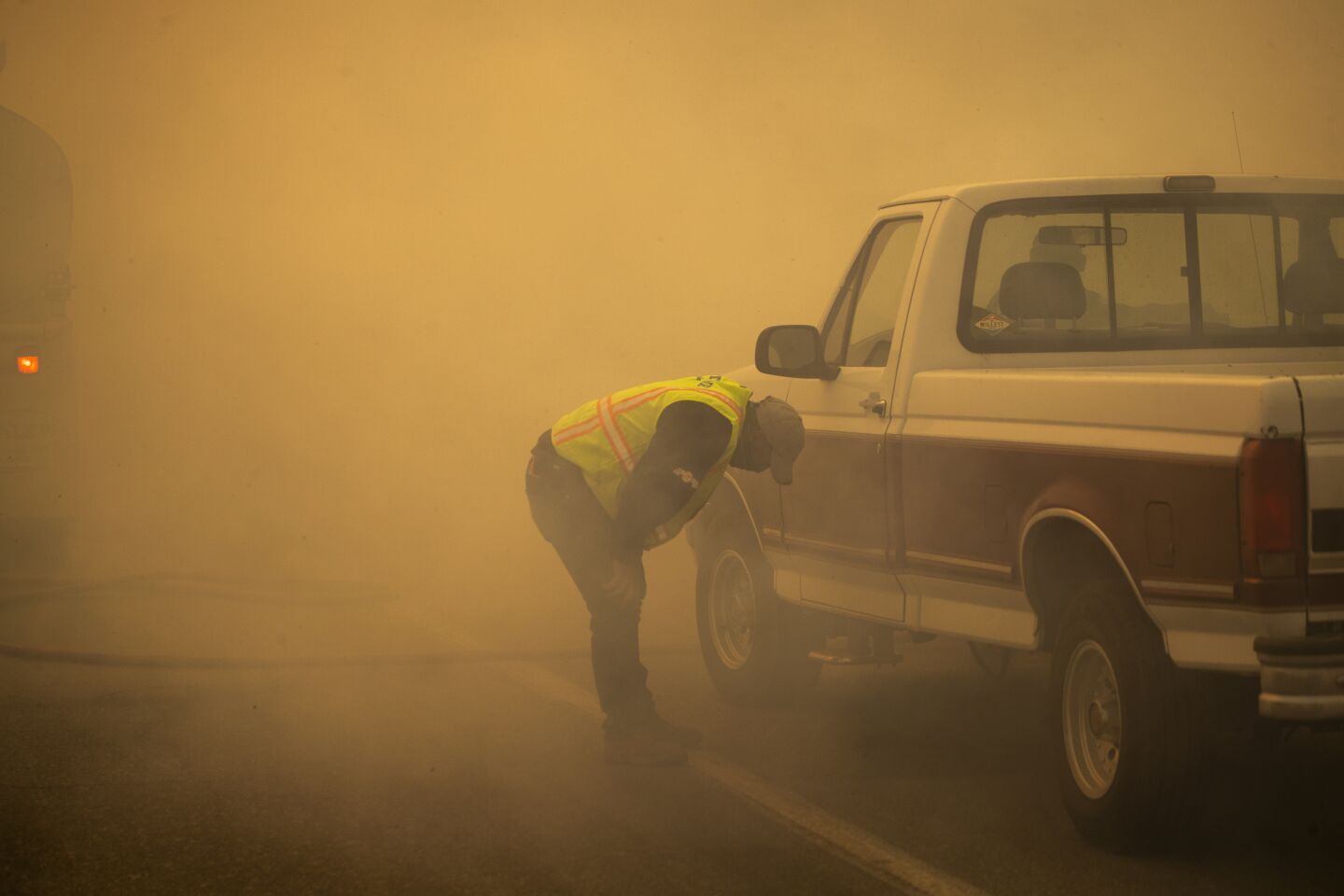 A man stands with his hands on his knees amid thick smoke
