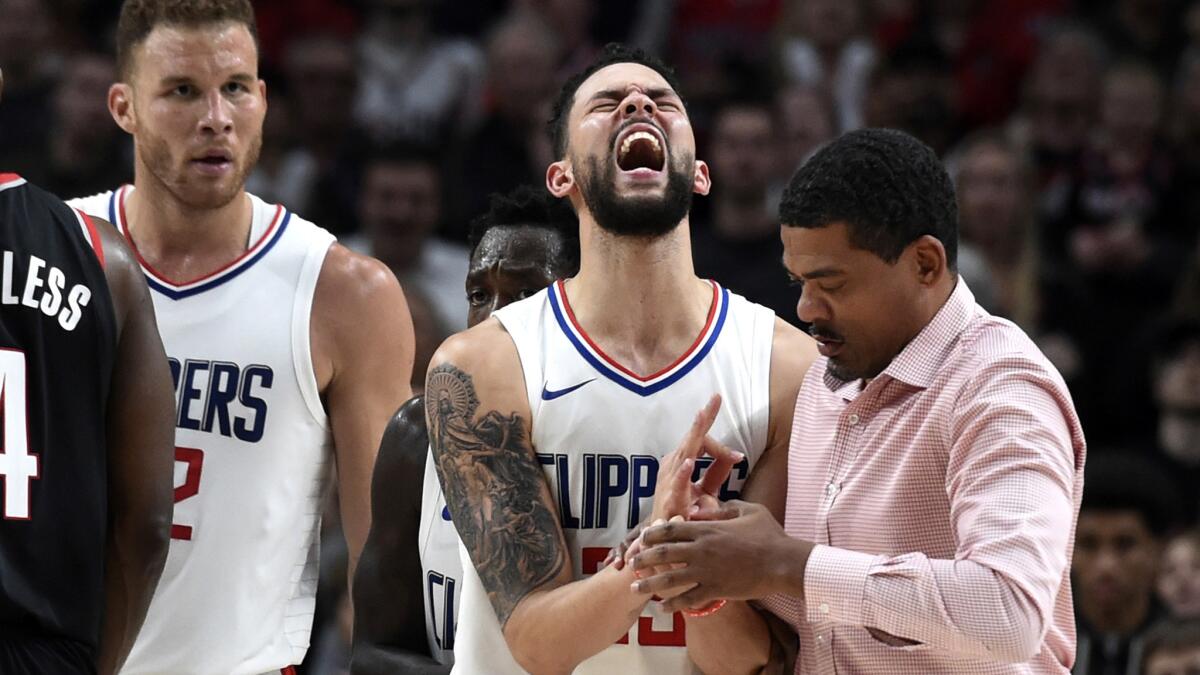 Clippers guard Austin Rivers is tended to by head athletic trainer Jasen Powell after dislocating the pinkie finger on his shooting hand on Thursday night in Portland.