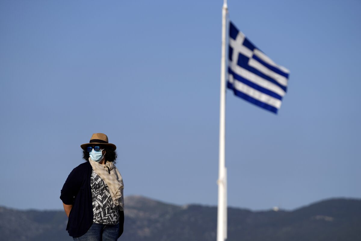 An employee of the Acropolis hill wearing protective face mask stands guard next of a Greek flag during a media tour for the Foreign Correspondents organised by the Greek Cultural Ministry at the Acropolis hill in Athens, Tuesday, June 8, 2021. Following last year's COVID-19 travel restrictions, tourism-reliant Greece is hoping to see a significant uptick in tourist arrivals this summer, and has expanded its list of nationalities allowed in for non-essential travel to include 23 countries – among them the U.S., the U.K. and China – as well as members of the European Union and the Schengen passport-free travel zone. (AP Photo/Thanassis Stavrakis)