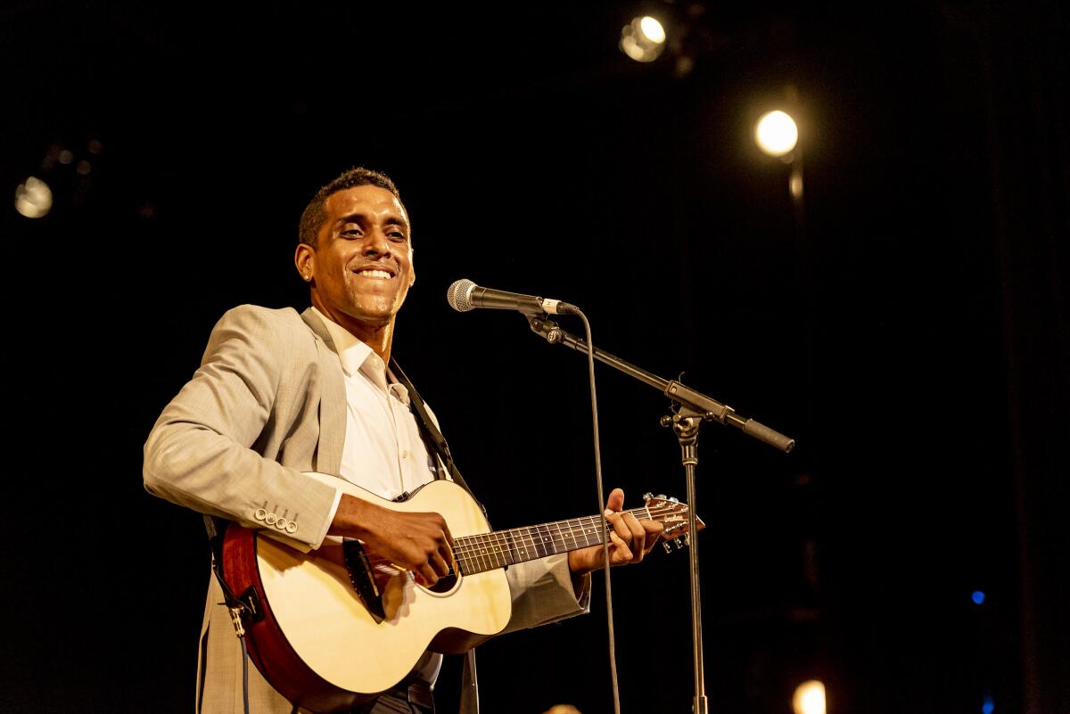 A man in a tan suit playing an acoustic guitar in front of a microphone on a stage
