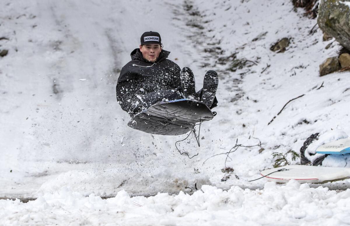 A teen on a sled lifts off while sliding down snow