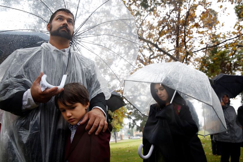 LOS ANGELES, CALIFORNIA-DECEMBER 4, 2019: Dev Kumar with his son William and daughter Beatrice, front left and right, stand during a ceremony to remember the 1,457 individuals cremated in 2016 whose remains have stayed in the county's possession for the past three years on December 4, 2019, at the L.A. County Crematory and Cemetery in Los Angeles, California. Reasons the dead go unclaimed can vary but some reasons are that they had no next of kin, they lost touch with their families or their families cannot pay to reimburse the cremation fee. (Photo By Dania Maxwell / Los Angeles Times)