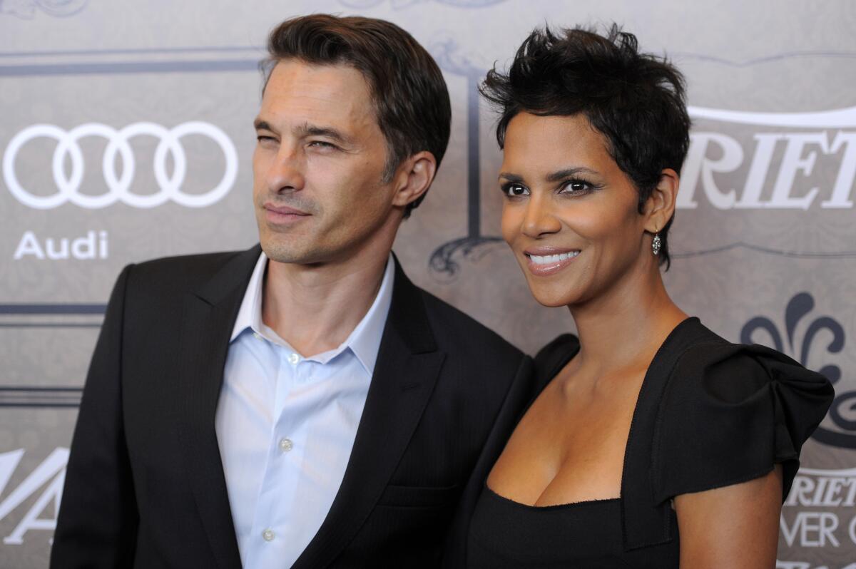 Olivier Martinez in a dark suit jacket and open-collar button-down standing close to Halle Berry, clad in a black dress