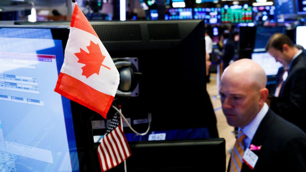 A small Canadian flag and U.S. flag are displayed alongside traders working on the floor of the New York Stock Exchange.