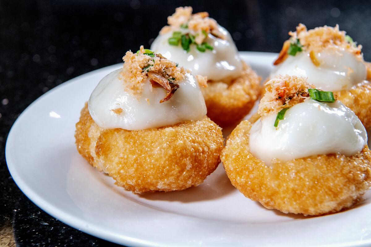 Round fried dumplings topped with a white sauce and chives