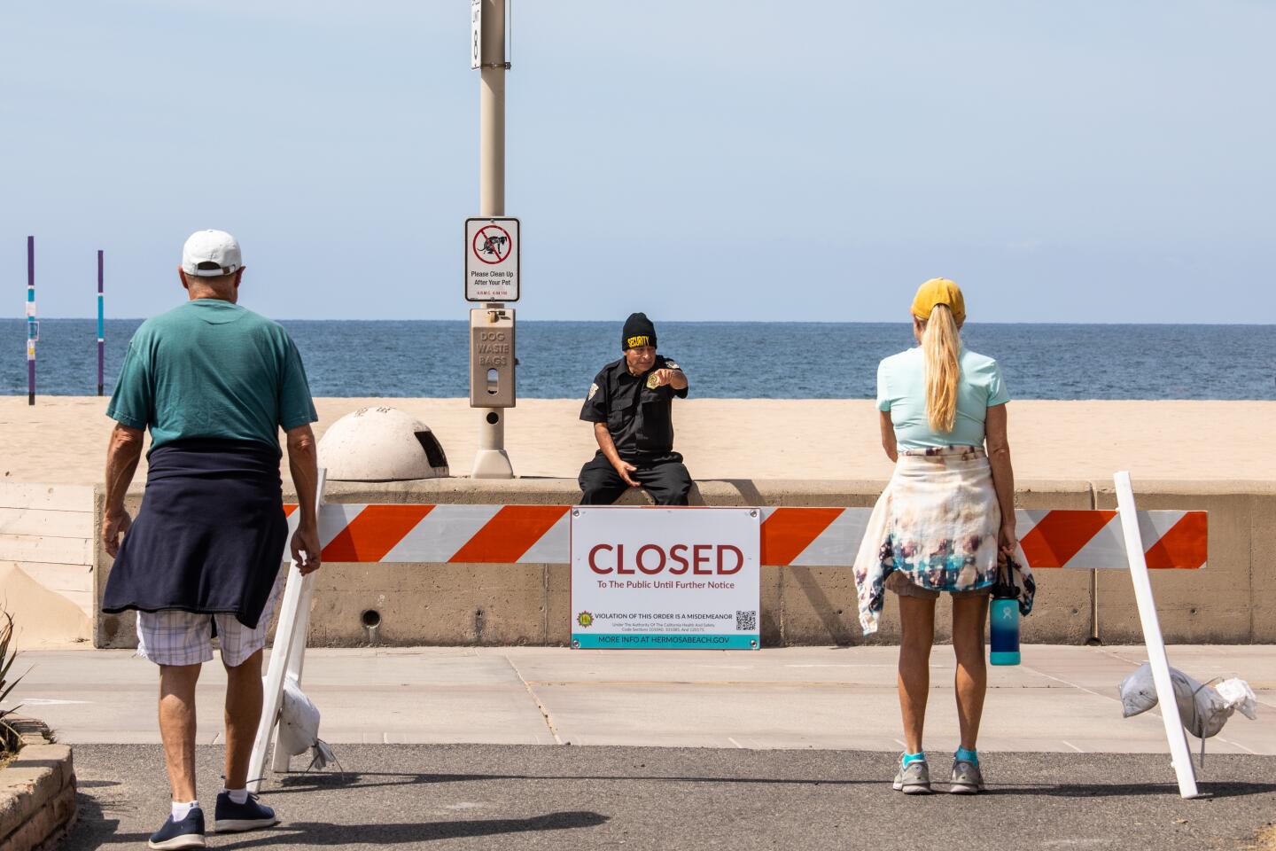 HERMOSA BEACH, CA --MARCH 28, 2020 - An unidentified worker with Absolute Intl. Security, providing security for the Hermosa Beach Police Department in closing off The Strand and two-mile stretch of Hermosa Beach, CA, lets people know of the closures, in an effort to prevent crowds and gatherings of people in the south bay town and slow the spread of the coronavirus, March 28, 2020. What began as only a city of Hermosa Beach, beach closure, quickly became a Los Angeles County beaches closure by late morning on Friday March 27, 2020, in an effort to slow the spread of the coronavirus. (Jay L. Clendenin / Los Angeles Times)