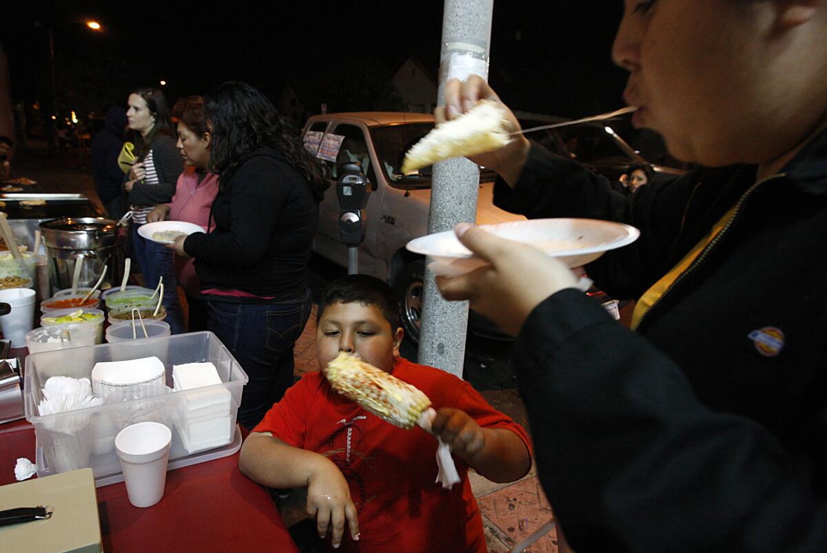 Boyle Heights residents dine at a sidewalk food stall along Cesar Chavez Boulevard.
