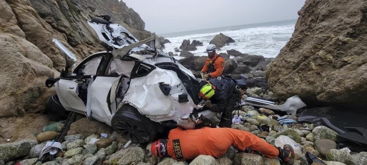 Emergency personnel examining damaged vehicle on rocks on beach