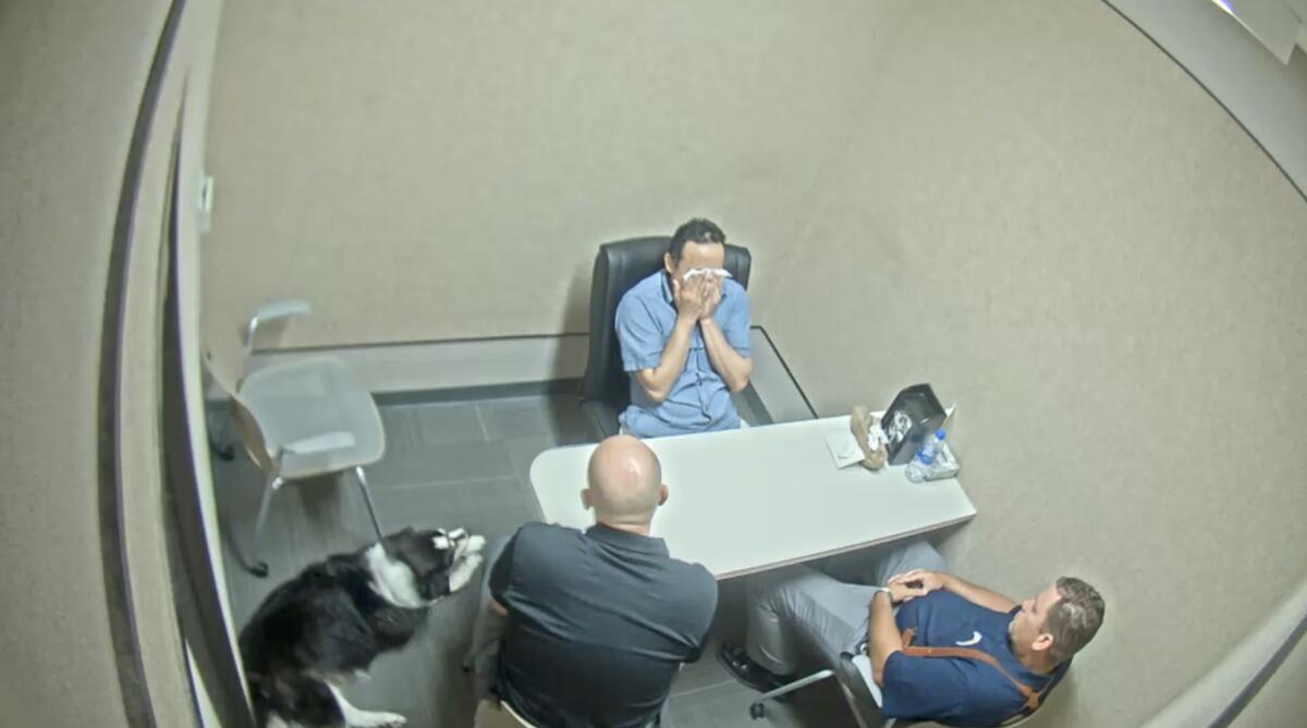 A man weeps while sitting with police in an interrogation room. 