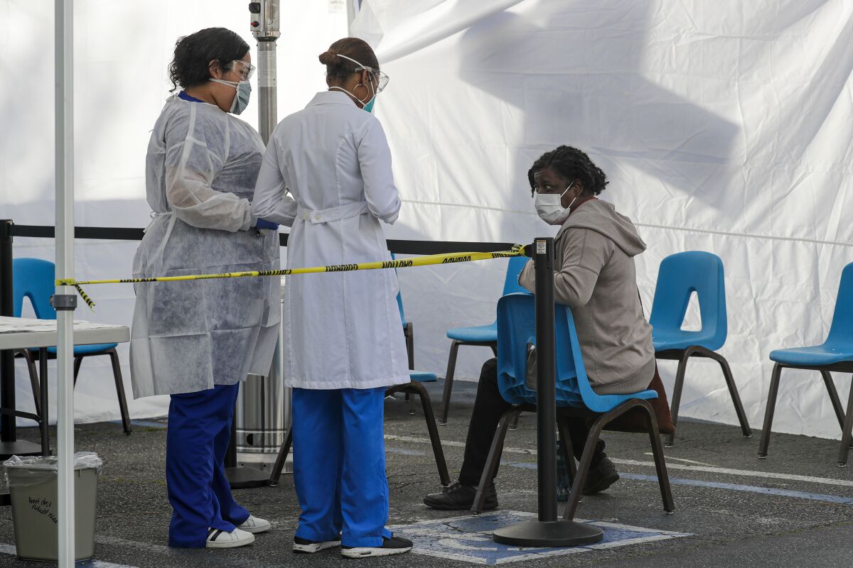 Healthcare workers check patient Netia Jone at a screening station for COVID-19 set up at the Watts Health Center.