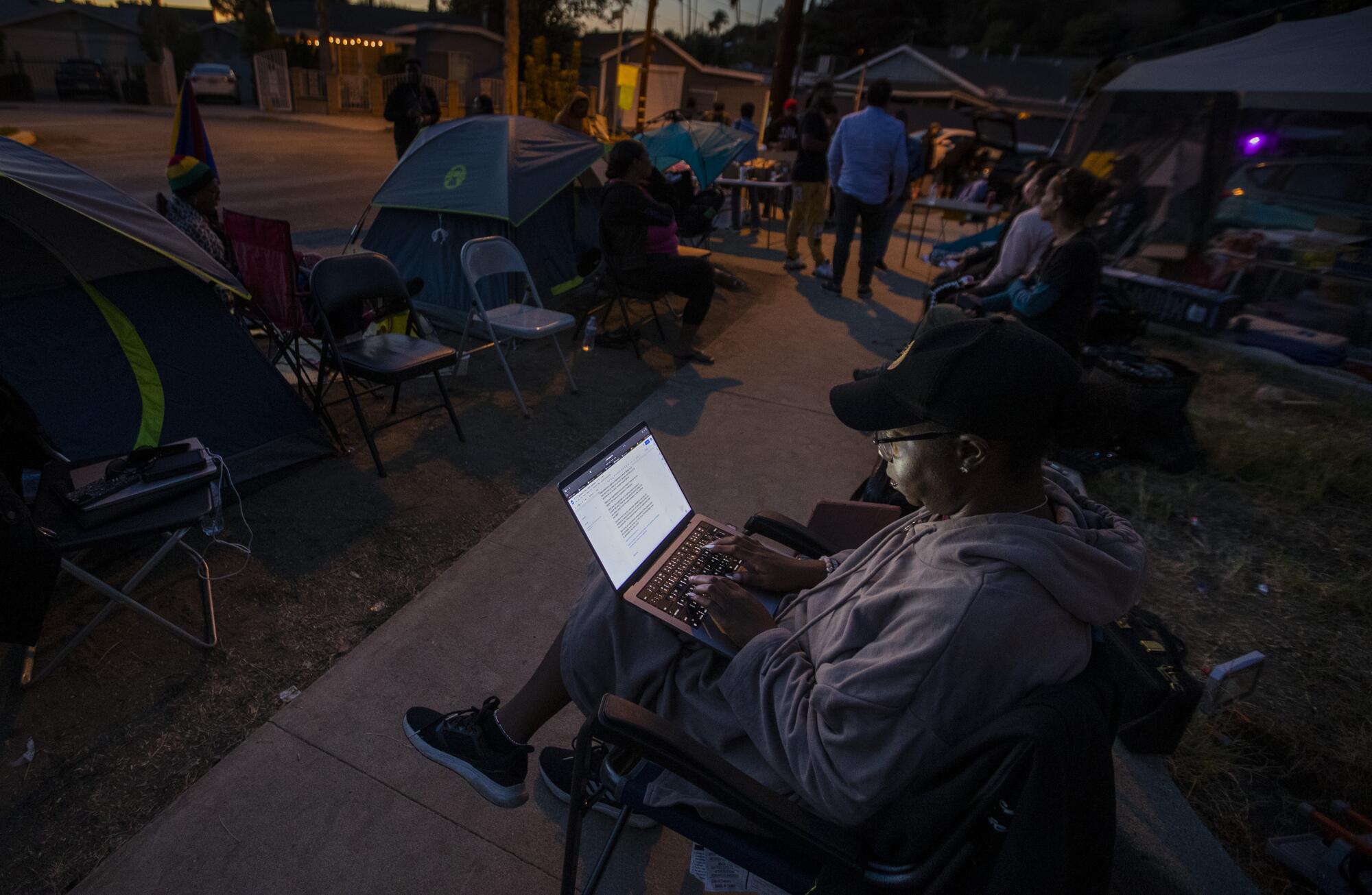 As evening falls, one activist works on her laptop as others gather outside tents.