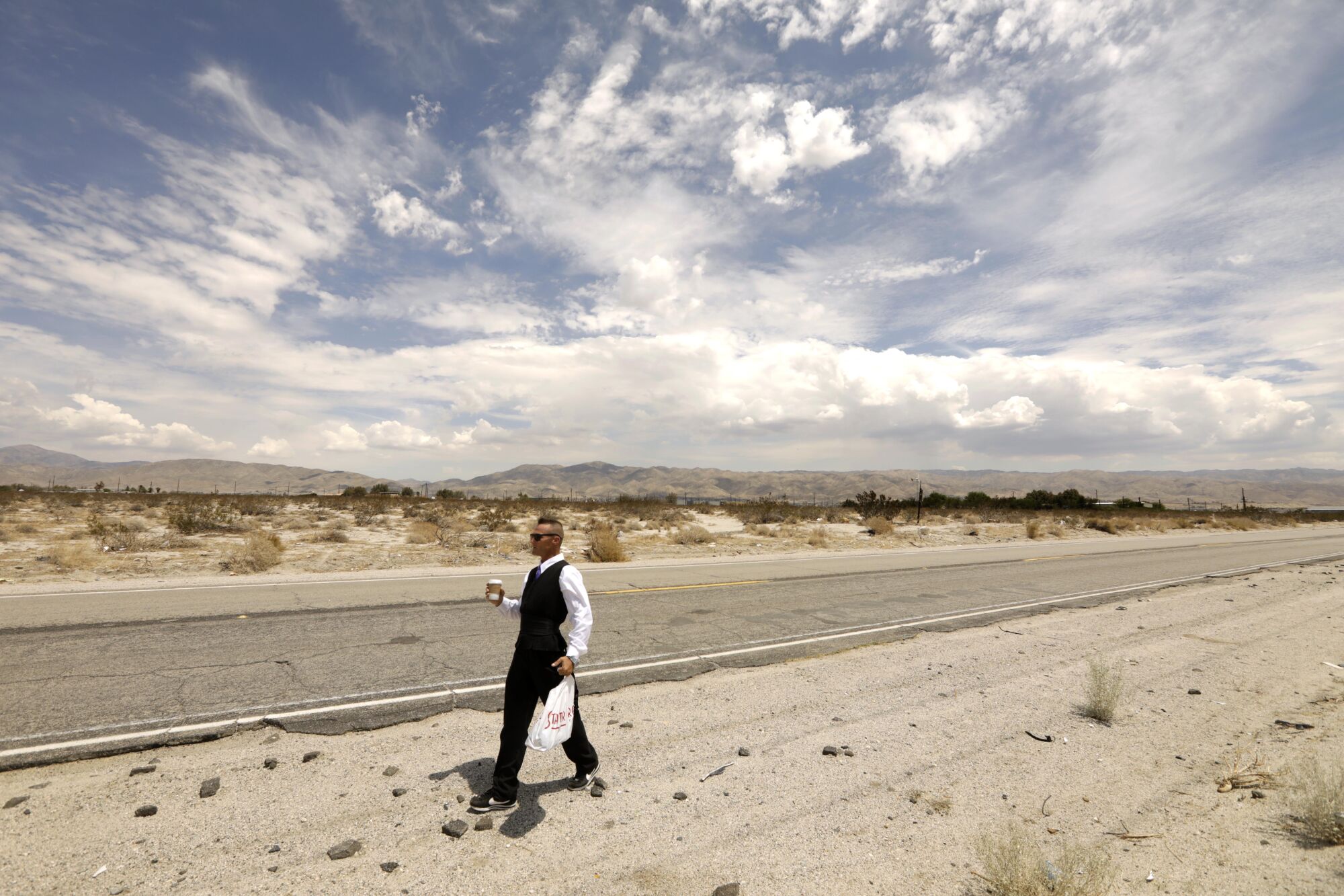July 27: Roger Embrey walks to a job interview along a road in the desert with clouds in the sky