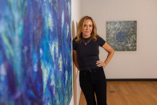 Denise Di Novi stands next to one of her paintings, an abstract  swirl of blues and greens.