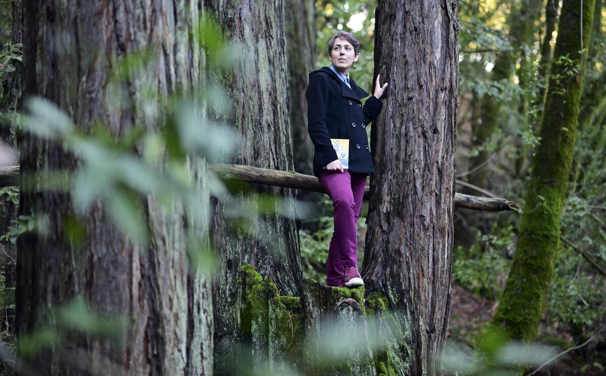 Maia Kobabe stands on a tree with her book "Gender Queer: A Memoir"