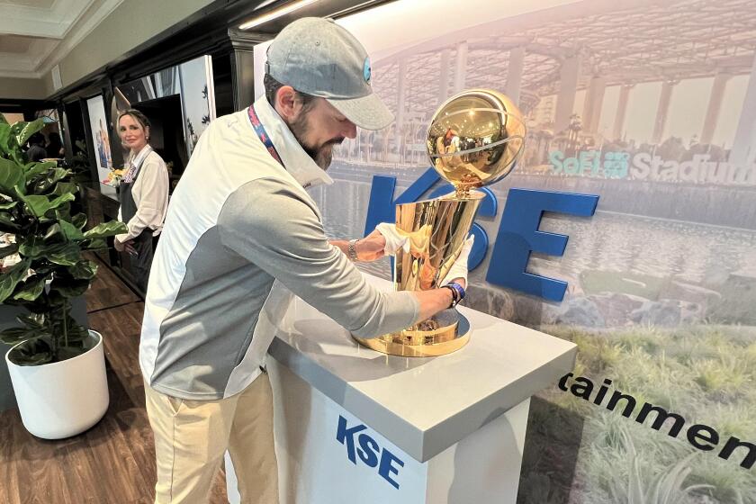 Josh Kroenke places the Larry O'Brien Trophy on a pedestal at the U.S. Open.