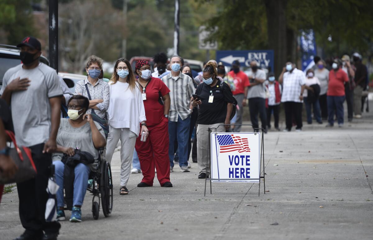 People wait in a long line next to a sign with an American flag that reads Vote Here