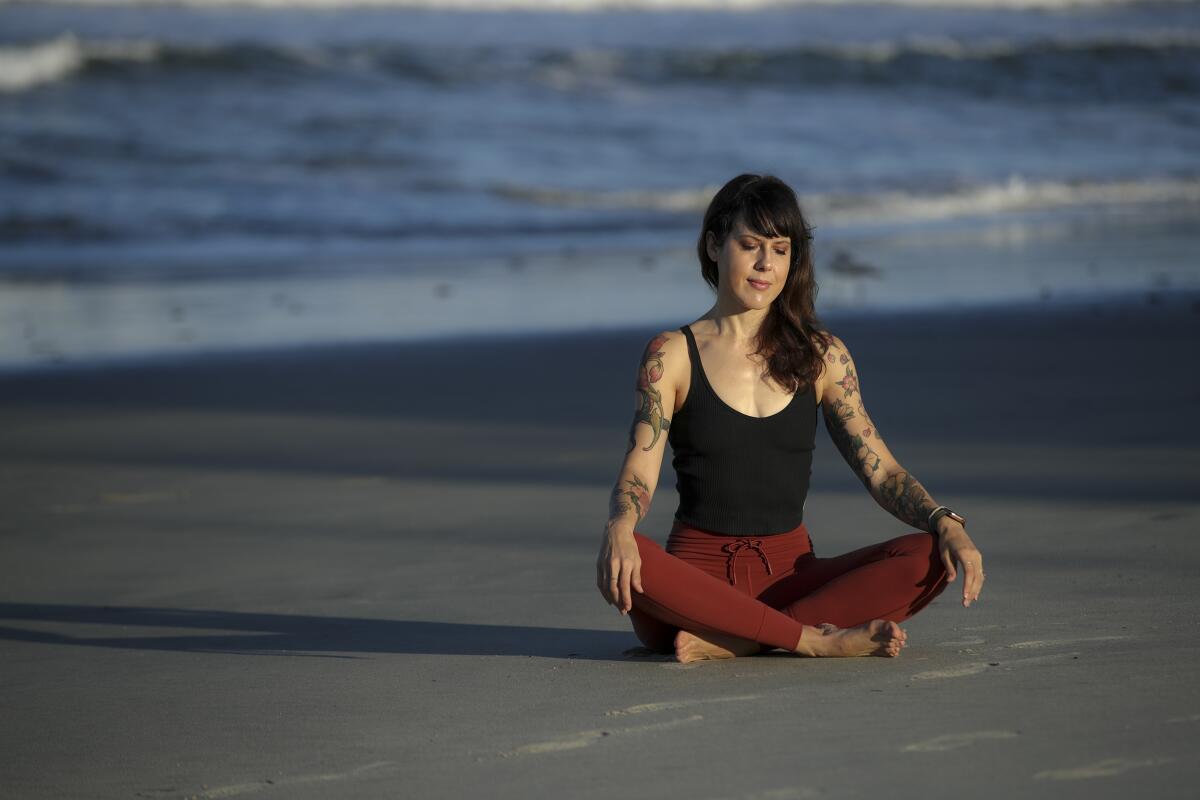 Yoga teacher Laura Schwartz sits cross-legged on the beach.