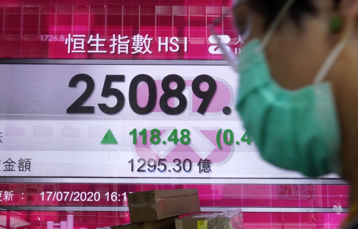 A man wearing a face mask walks past a bank's electronic board showing the Hong Kong share index at Hong Kong Stock Exchange Monday, July 20, 2020. Asian shares were mostly lower Monday as investors cautiously eyed the summit of European leaders discussing the pandemic crisis and coronavirus cases continued to soar in the U.S.(AP Photo/Vincent Yu)