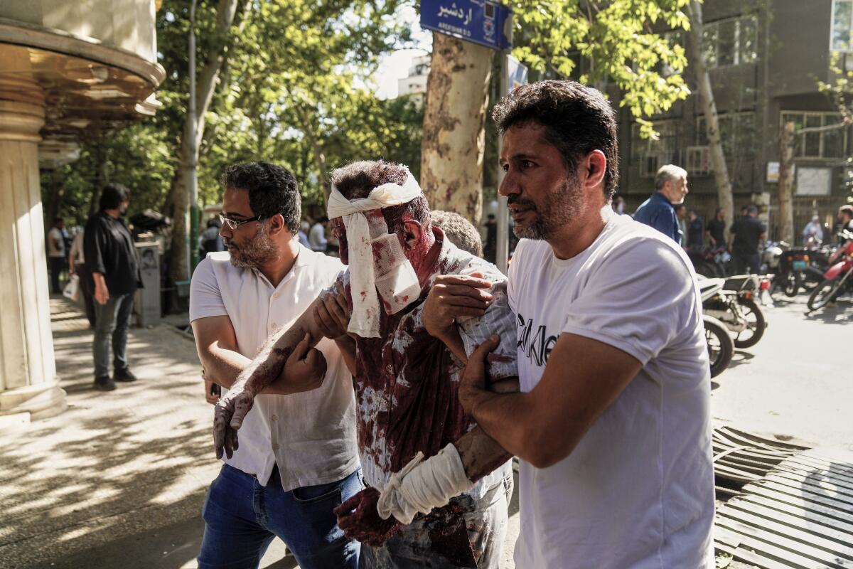 Two men assist a bloodied and bandaged man.