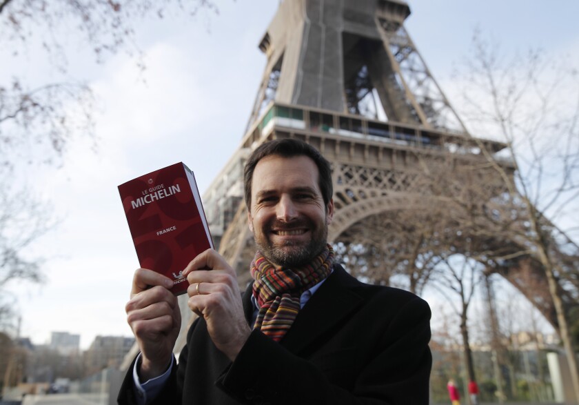 Gwendal Poullennec, head of Le Guide Michelin, poses outside the Eiffel Tower with the 2021 edition Monday, Jan. 18, 2021 in Paris. Michelin will later announce the 2021 winners in a broadcast from the Eiffel Tower. (AP Photo/Francois Mori)