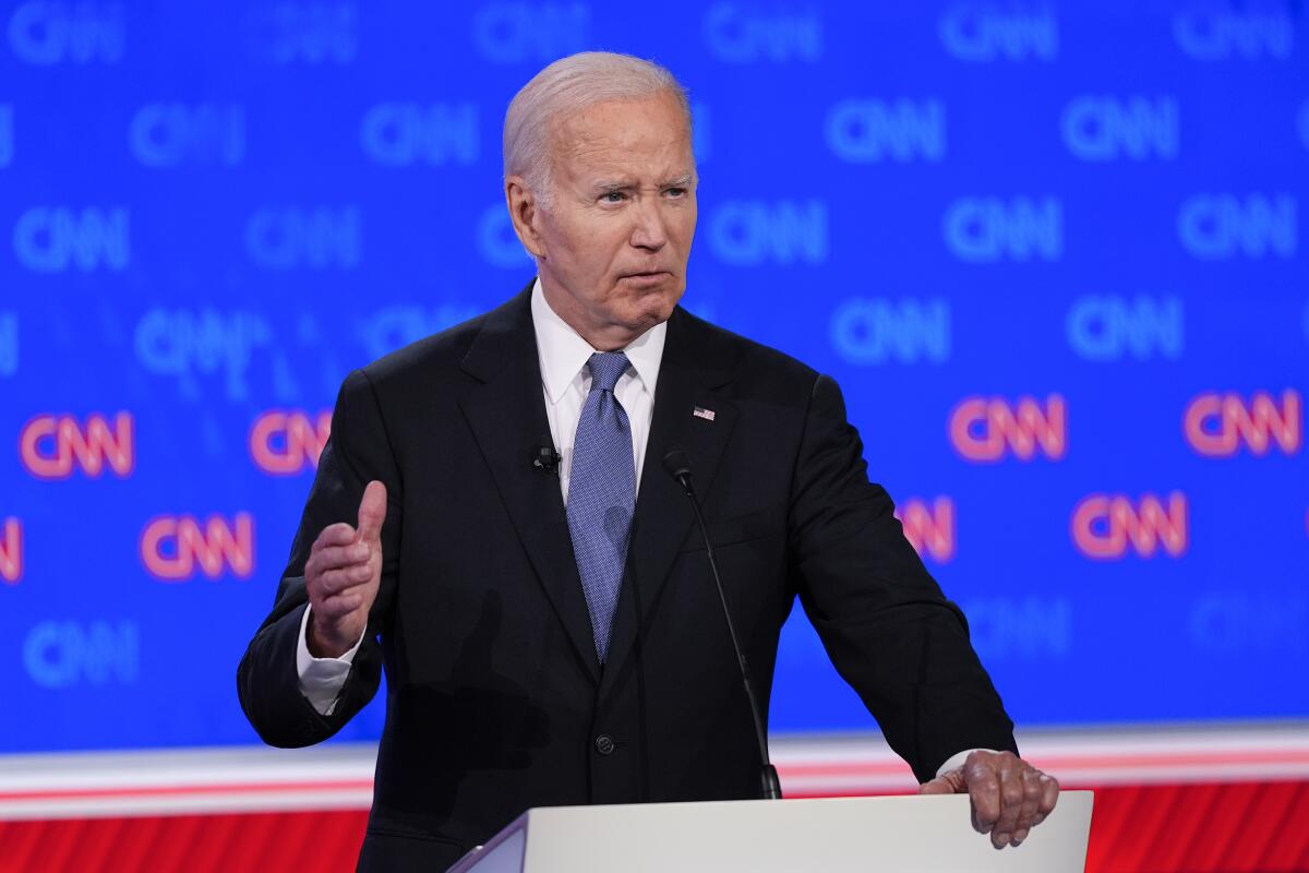President Biden raises a hand at the CNN debate lectern.