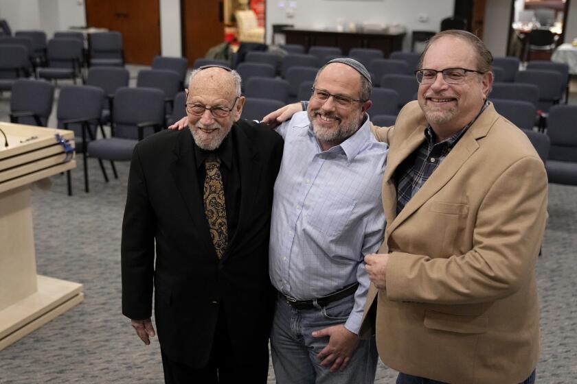 In this Dec. 22, 2022, photo, Lawrence Schwartz, left, Shane Woodward, center, and Jeff Cohen, right, smile as they pose for a photo inside Congregation Beth Israel in Colleyville, Texas. A year ago, a rabbi and three others survived a hostage standoff at their synagogue in Colleyville, Texas. Their trauma did not disappear, though, with the FBI's killing of the pistol-wielding captor. Healing from the Jan. 15, 2022, ordeal is ongoing. (AP Photo/Tony Gutierrez)