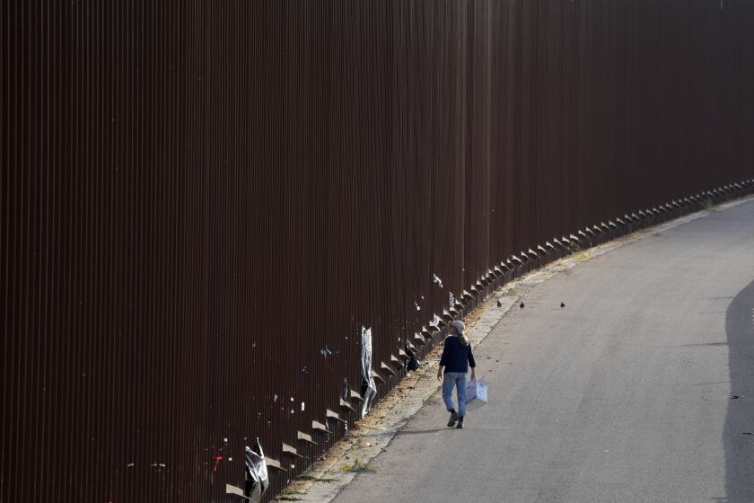 Un voluntario camina al lado del muro fronterizo en San Diego mientras entrega pañales a migrantes que esperan para solicitar asilo en Estados Unidos el jueves 11 de mayo de 2023. (AP Foto/Gregory Bull)