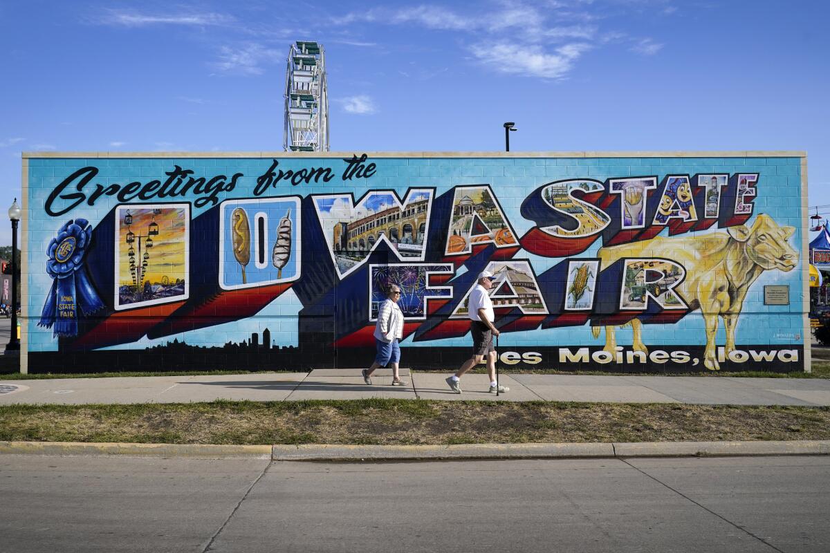 Fairgoers walk past a mural at the Iowa State Fair, Friday, Aug. 19, 2022, in Des Moines, Iowa. Potential White House hopefuls from both parties often swing by Iowa's legendary state fair during a midterm election year to connect with voters who could sway the nomination process. But this year, the traffic at the fair was noticeably light. Democrats are uncertain about President Joe Biden's political future and many Republicans avoid taking on former President Donald Trump. (AP Photo/Charlie Neibergall)