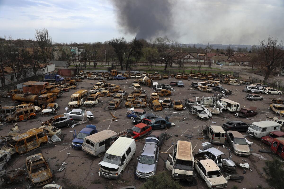 Smoke rises over a parking lot full of damaged and burned vehicles.