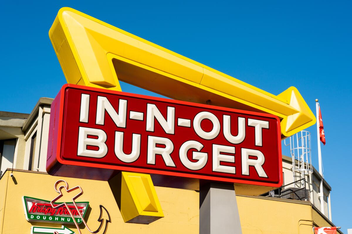 A sign with an arrow reads In-N-Out Burger. In the background is a Krispy Kreme Doughnuts sign.